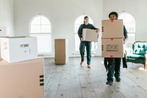 Two smiling movers carry furniture into a moving truck.